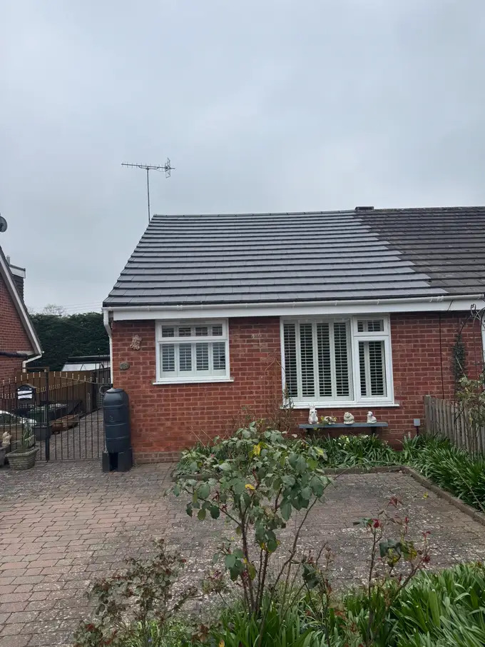 Semi-detached bungalow with a new grey tiled roof, the neighbouring half still in its original tiles
