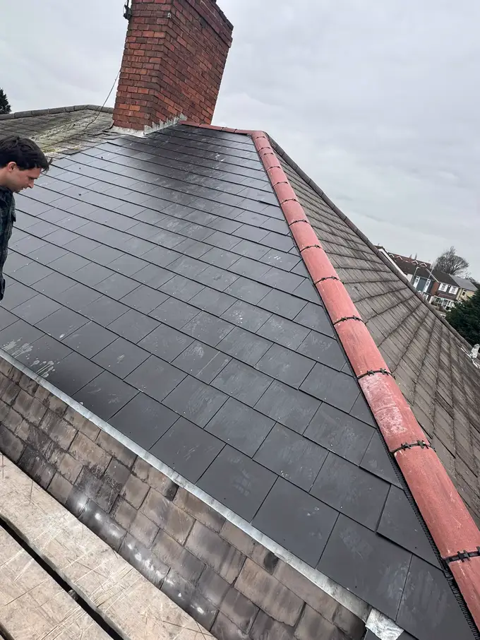 New slates laid on a pitched roof alongside the original tiles, with a red ridge