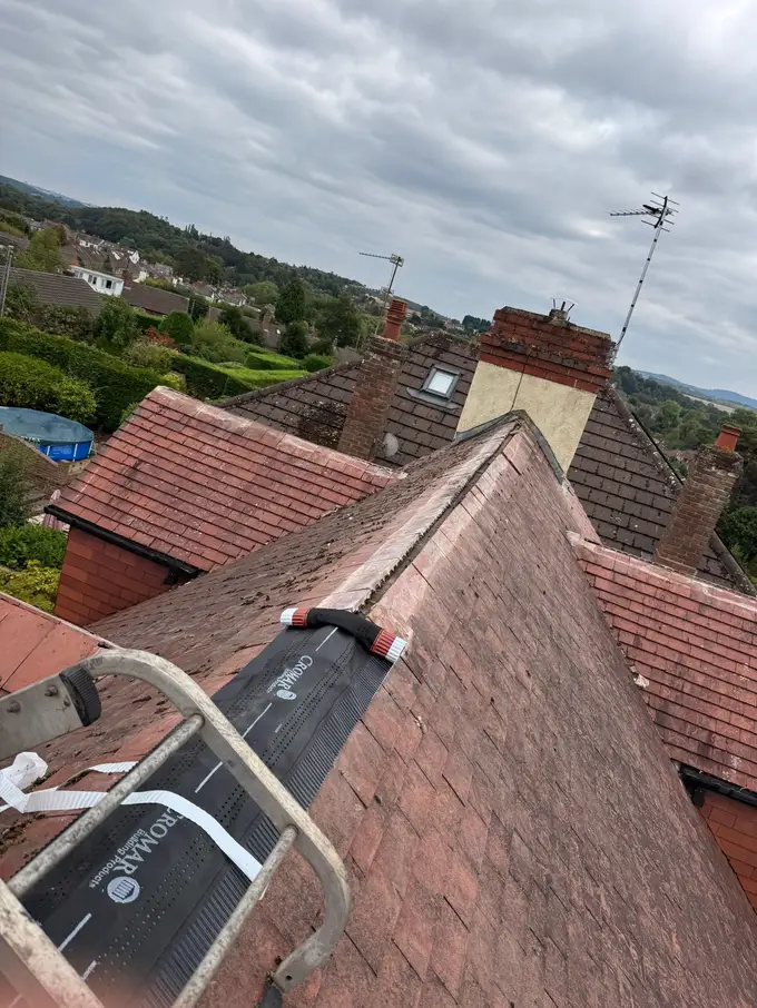 Dry ridge roll being fitted along the ridge of a red tiled roof, with a roof ladder hooked over the slope
